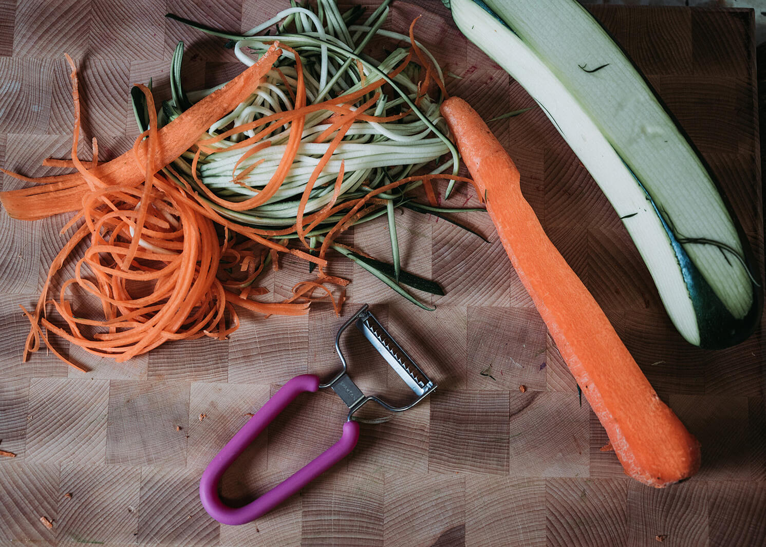 Spartan Shredder with extra-sharp Japanese-steel blades lays on a cutting board beside shredded carrot and zucchini