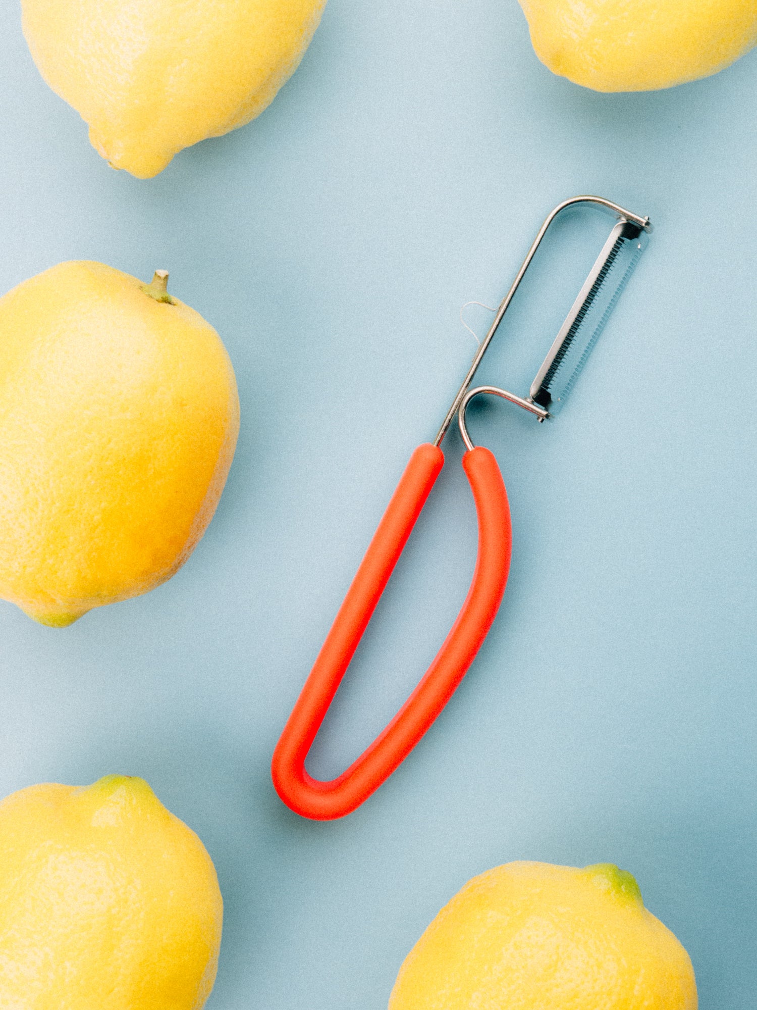 Spartan peeler with Japanese-steel blade and red ergonomic handle lays amongst lemons